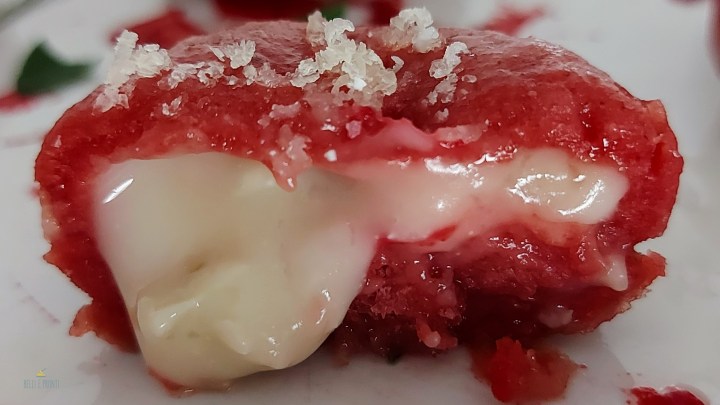 Uno gnocco di patate e rape rosse ripieno di gorgonzola tagliato per mettere in evidenza la cremosità del ripieno.