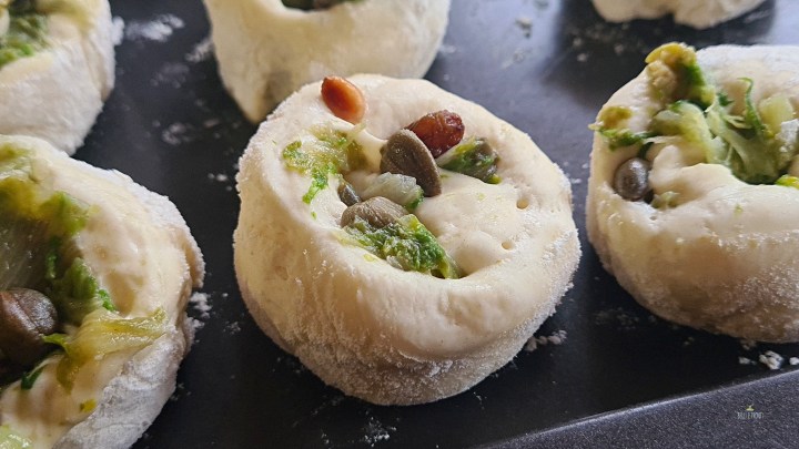 La versione monoporzione della pizza di scarole: un rotolo di pasta delle pizza farcito con la scarola insaportita con olio, aglio, acciughe e capperi, impreziosita da pinoli, uvetta e olive verdi.