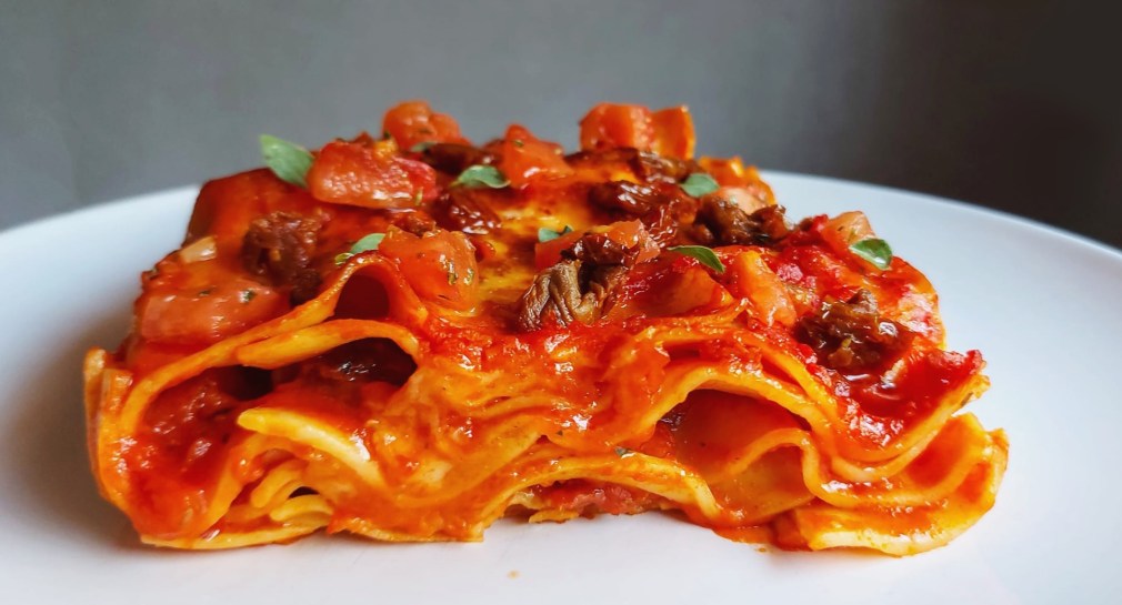 Sfoglia di lasagna classica condita con salsa di pomodori, pomodori freschi tagliati a dadini e pomodori secchi.
