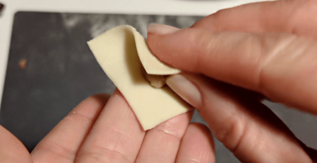 Come fare i tortellini: dopo avere messo il ripieno al centro di quadratini di pasta piegare i quadratini in modo da far combaciare angoli non adiacenti e creare un triangolo.