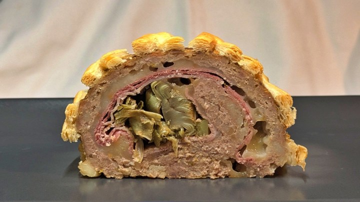 Fetta di polpettone in crosta farcito, polpettone farcito con prosciutto cotto, formaggio e carciofi. Polpettone al forno. Ricette con carciofi per Pasqua. Ricette tradizionali Pasqua. Pranzo di Pasqua.