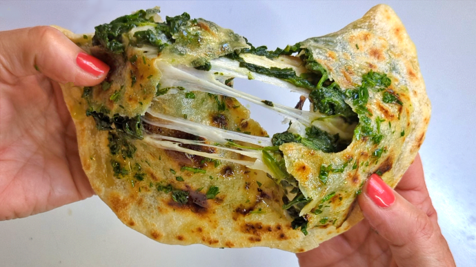 Particolare della farcitura dellaricetta di pane ripieno cotto in padella ispirata al gozleme turco: una sottilissima sfoglia di pane in cui proponiamo un ripieno di spinaci e provola affumicata, nappato con olio al prezzemolo. Filante e godurioso!